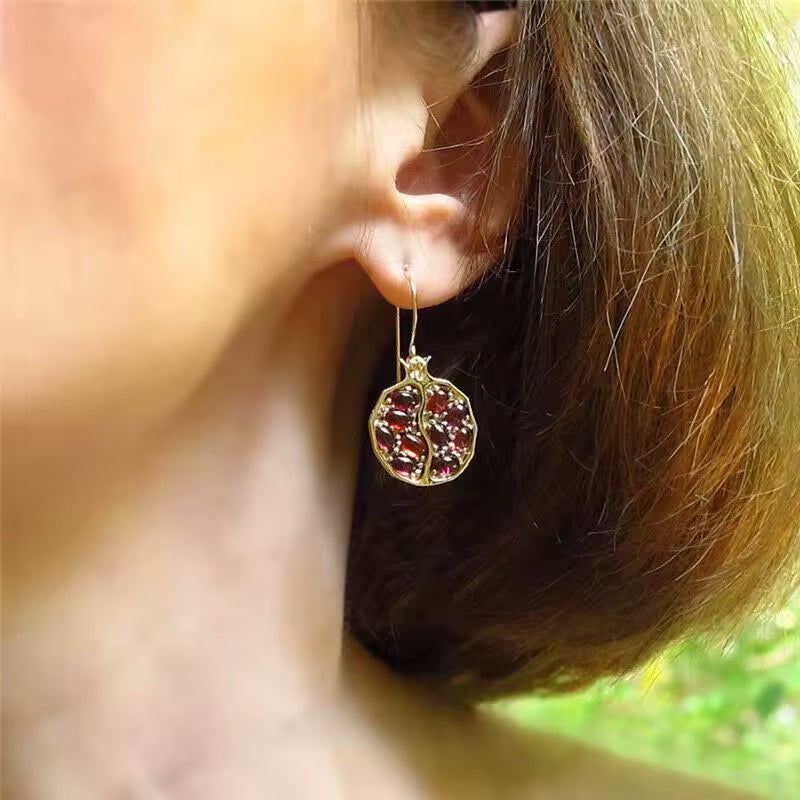 Close-up of a person wearing a gold earring with a red gemstone.