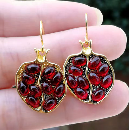 Gold earrings with red gemstones held between fingers against a blurred background